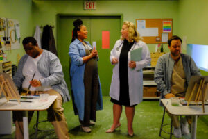 An greenish art room in a mental hospital. Two patients work while the art teacher and the clinic director talk.